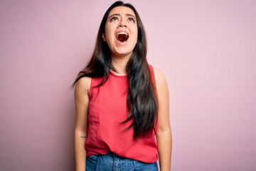 Wall Mural - Young brunette woman wearing casual summer shirt over pink isolated background angry and mad screaming frustrated and furious, shouting with anger. Rage and aggressive concept.