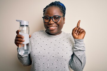 Sticker - Young african american plus size sportswoman with braids drinking bottle of water surprised with an idea or question pointing finger with happy face, number one