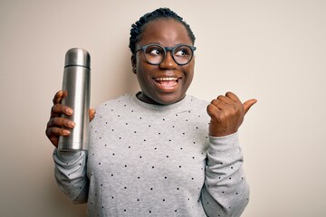 Sticker - Young african american plus size woman with braids holding thermo with coffee pointing and showing with thumb up to the side with happy face smiling