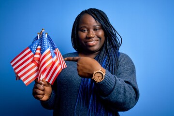 Sticker - Young patriotic african american plus size woman with braids holding united states flags very happy pointing with hand and finger