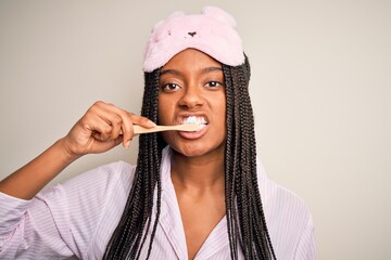 Canvas Print - Young beautiful african american woman wearing pajama and sleep mask brushing her teeth using tooth brush and oral paste, cleaning teeth and tongue as healthy health care morning routine