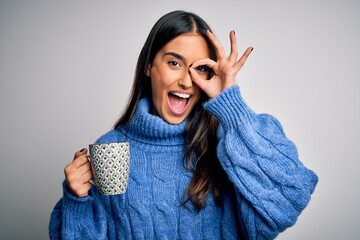 Wall Mural - Young beautiful brunette woman drinking cup of coffee over isolated white background with happy face smiling doing ok sign with hand on eye looking through fingers