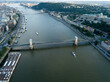 Aerial view of Széchenyi Chain Bridge over Danube river near Parliament palace in Budapest city, Hungary. Cars drive on bridge, road, boats floating on river, ships moored near riverside. Historic cen
