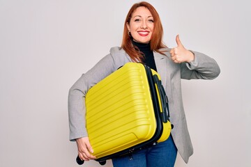 Sticker - Young beautiful redhead woman holding suitcase prepared to business travel happy with big smile doing ok sign, thumb up with fingers, excellent sign