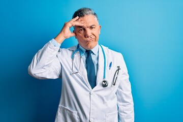 Poster - Middle age handsome grey-haired doctor man wearing coat and blue stethoscope worried and stressed about a problem with hand on forehead, nervous and anxious for crisis