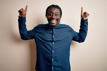 Sticker - Young handsome african american man wearing casual shirt standing over white background smiling amazed and surprised and pointing up with fingers and raised arms.