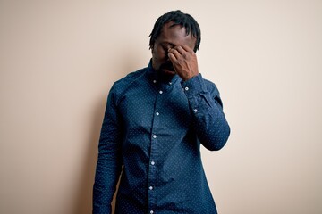 Sticker - Young handsome african american man wearing casual shirt standing over white background tired rubbing nose and eyes feeling fatigue and headache. Stress and frustration concept.