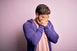 © Krakenimages.com - Young blond man with beard and blue eyes wearing purple sweatshirt over pink background with sad expression covering face with hands while crying. Depression concept.