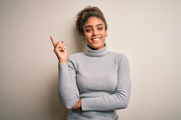 Canvas Print - Beautiful african american girl wearing turtleneck sweater standing over white background with a big smile on face, pointing with hand and finger to the side looking at the camera.