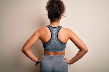 Wall Mural - Young african american sportswoman doing sport wearing sportswear over white background standing backwards looking away with arms on body