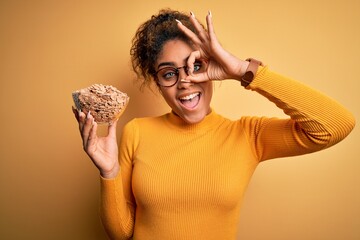 Poster - Young african american girl holding bowl with healthy cornflakes cereals over yellow background with happy face smiling doing ok sign with hand on eye looking through fingers