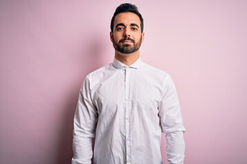 Poster - Young handsome man with beard wearing casual shirt standing over pink background Relaxed with serious expression on face. Simple and natural looking at the camera.