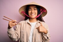 Young Thai Woman Wearing Traditional Conical Asian Hat Eating Food Using Chopsticks With Surprise Face Pointing Finger To Himself