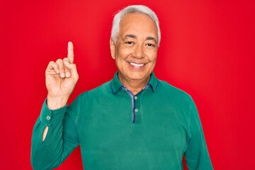 Wall Mural - Middle age senior grey-haired man wearing casual sweater over red isoalted background pointing finger up with successful idea. Exited and happy. Number one.