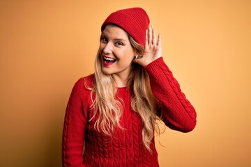 Canvas Print - Young beautiful blonde woman wearing casual sweater and wool cap over white background smiling with hand over ear listening an hearing to rumor or gossip. Deafness concept.