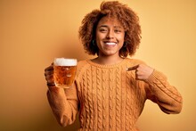 Young Beautiful African American Afro Woman With Curly Hair Drinking Jar Of Beer With Surprise Face Pointing Finger To Himself