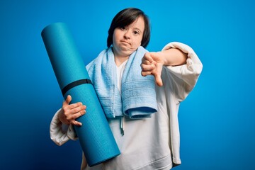 Sticker - Young down syndrome fitness woman training yoga and pilates holding workout mat with angry face, negative sign showing dislike with thumbs down, rejection concept