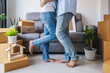© Kittiphan - Happy young couple hugs dancing in living room at new house with stack of cardboard boxes on moving day