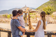 © galitskaya - Happy mother, father and son watching and feeding giraffe in zoo. Happy family having fun with animals safari park on warm summer day