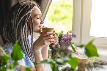 A cute young woman is enjoying an aromatic coffee on a sunny summer morning. Concept of a dreamy mood, a cozy atmosphere and a pleasant start to the day