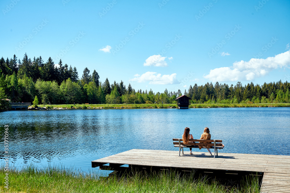 Zwei Frauen am See genießen den Sommer auf dem Steg  - obrazy, fototapety, plakaty 
