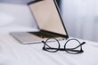 Picture of eyeglasses and laptop on bed in bedroom. Selective focus on eyeglasses.