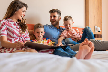 Wall Mural - family of four enjoying together at hotel room, sitting at bed reading hotels offers.