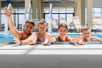 Wall Mural - portrait of smiling family of four having fun and relaxing in indoor swimming pool at hotel resort.