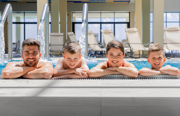 Wall Mural - portrait of smiling family of four having fun and relaxing in indoor swimming pool at hotel resort.