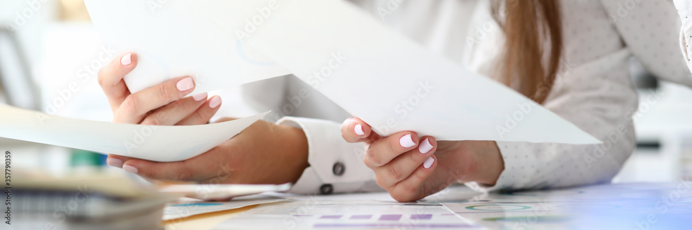 Focus on tender female hands holding important business documents with significant charts and graphs used for special corporation analysis. Accounting office concept. Blurred background - obrazy, fototapety, plakaty 