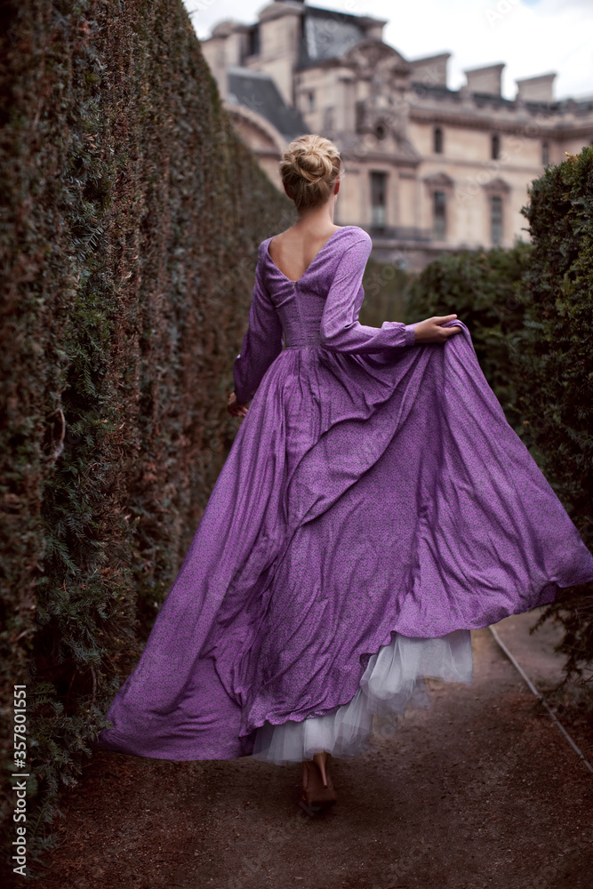 A beautiful blonde girl model runs in a purple long flowing dress in a maze  park in Paris, surrounded by green bushes Stock Photo | Adobe Stock