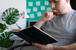 © Ramil Gibadullin - Man takes break from work, sits in his living room and reads book. Part of the body and the book close up. Digital detox concept. Horizontal orientation.