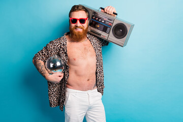 Photo of cool macho guy naked torso sunny hot day hold retro tape recorder shoulder glitter disco ball chill rest party wear shorts leopard shirt sun specs isolated blue background