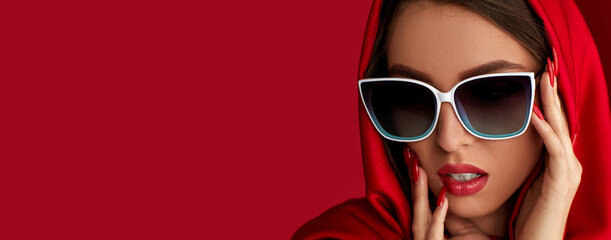 Wall Mural - gorgeous brunette woman with luxurious make-up in white sunglasses and red headscarf on red background. copy space for text