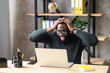 Emotional happy African-American man holding head with his hands and screams excited from good news or deal, he looks at laptop screen with triumph