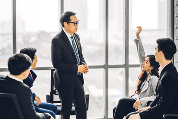 Businessman standing in front of group of people in consulting meeting conference seminar and showing hand to answer question at hall or seminar room.presentation and coaching concept