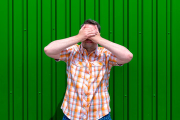 Man covers his face with his hands.Trendy bright green outdoor background