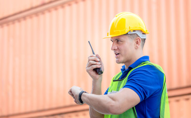 Wall Mural - Engineer man in hardhat and safety vest talks on two-way radio, Worker man looking at the watch time at containers cargo