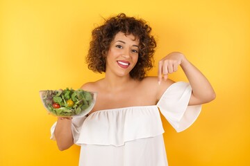 Wall Mural - Charming emotive caucasian woman pointing down or at her shirt while smiling joyfully and expressing positive emotions over white background. Girl trained a lot, she wants to show her muscles