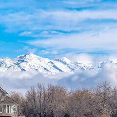 Square crop Peaks of a magnificent snowy mountain over low puffy clouds against blue sky