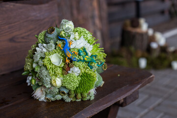 
Bridal bouquet in green colors with decors in the form of two lizards of blue and green lies on a wooden background.