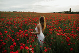 Fototapeta Kuchnia - Tender woman in white dress standing in poppy field and enjoying beautiful landscape. Relaxing in nature during summer evening. Atmospheric authentic moment. Copy space.