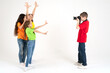 © Luiza - A boy photographer takes pictures of three cute girls in bright T-shirts on a white background in the studio. Young photographer and blogger. School of photography for children