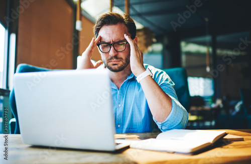 Businessman feeling headache while doing distance work in coffee shop