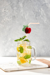 Citrus lemonade or mojito cocktail with lemon and orange and basil. Cold beverage or drink with ice on marble cutting board