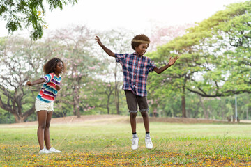 Wall Mural - Happy young boy and girl paying in the park. Two African American children having fun with jumping over the rope in the garden. Education or Field trip concept