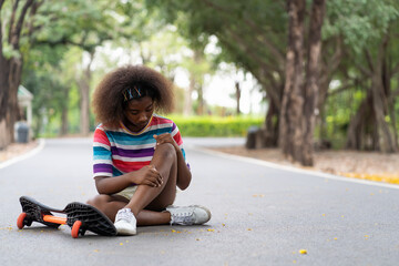 Wall Mural - African American young girl fell to the ground while practicing skateboarding on the street in the park.