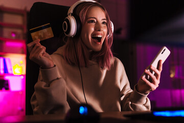 Wall Mural - Image of excited girl holding credit card and using cellphone