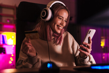 Wall Mural - Image of excited girl holding credit card and using cellphone