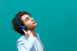 © 5M - I am flying away from this music. Portrait of a young beautiful man presses one dimanic of blue headphones at his ear and throwing head back to enjoying sounds